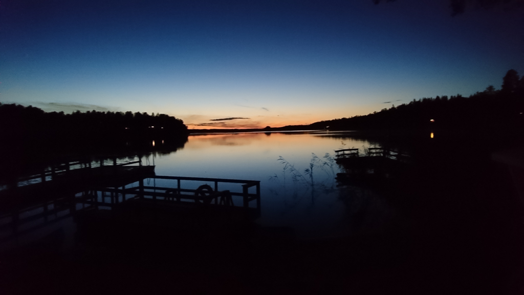 Solnedgång över en sjö, med mörka silhuetter av bryggor och skog.