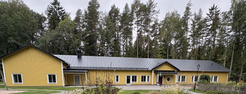 Det nybyggda annexet på Tallkrogen, en gul träbyggnad med plåttak omgiven av tallskog och planteringar.