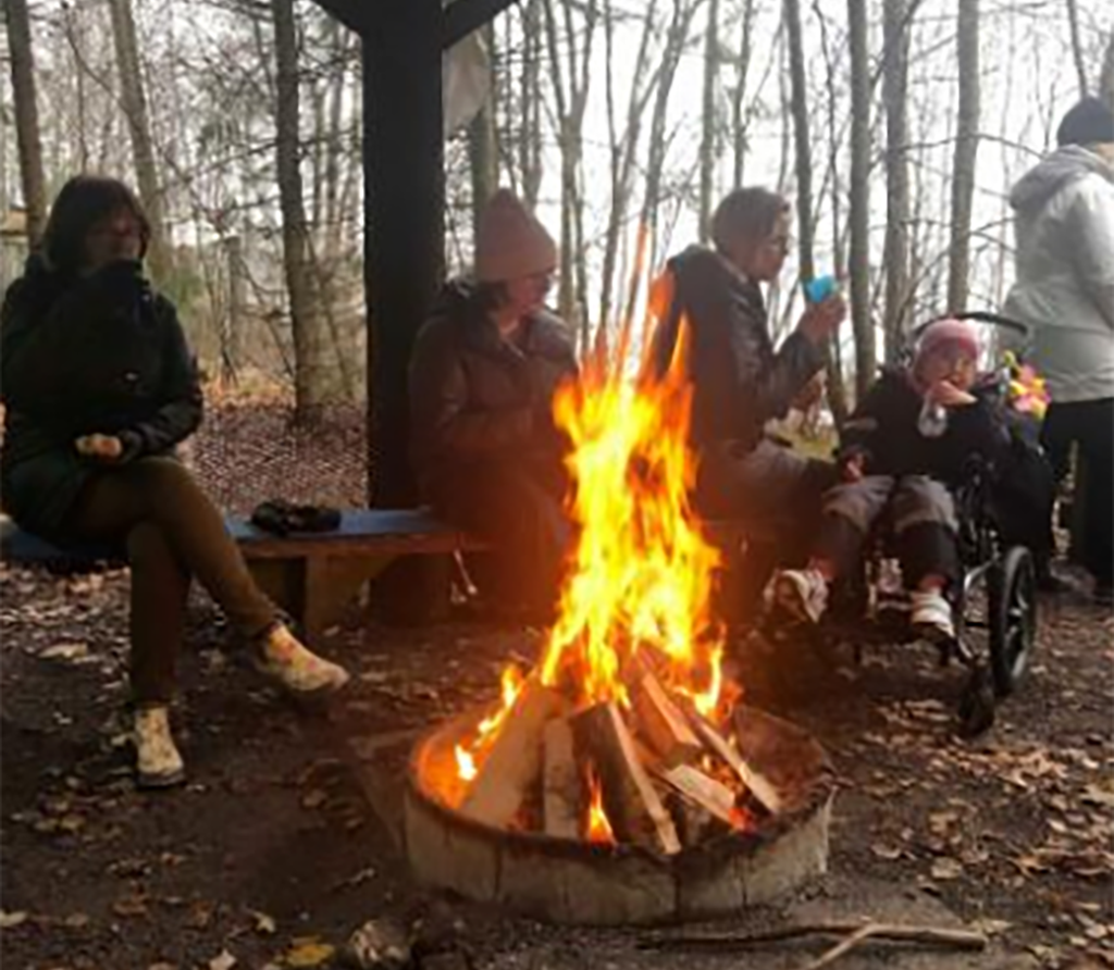 Grupp människor som sitter runt en eld utomhus i skogsmiljö.